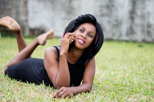 Close-up of young woman in black dress is lying in the garden talking on the phone