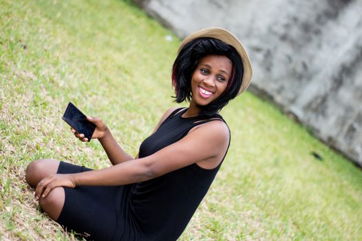 smiling young woman sitting alone in a park and holding a telephone in hand