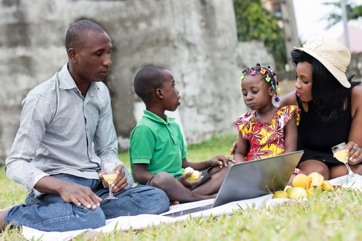 happy family sitting in the garden with breakfast and looking on laptop