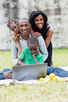happy family sitting at the park in front of a computer and playing in a group