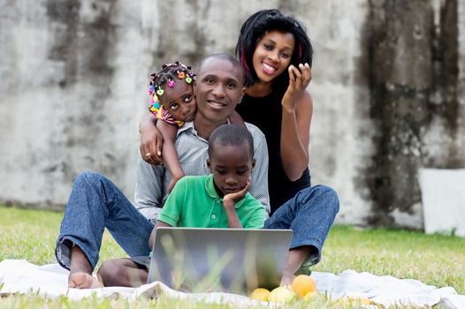 happy family sitting at the park and looking together on a laptop