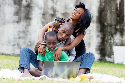 portrait of a family sitting at the park playing together in front of a computer