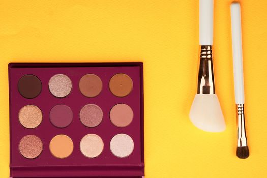 Eyeshadows and makeup brushes on a yellow background top view professional cosmetics. High quality photo