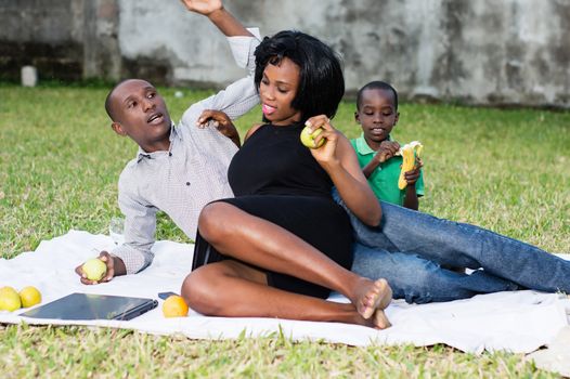 happy couple sitting at the park with their son and eating a green apple in love