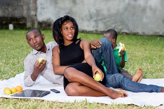 happy couple sitting at the park with their son and eating a green apple in love