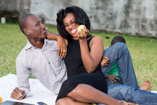 happy couple sitting at the park with their son and eating a green apple in love