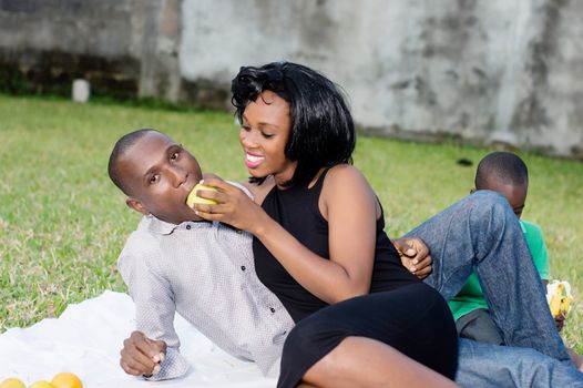 happy couple sitting at the park with their son and eating a green apple in love