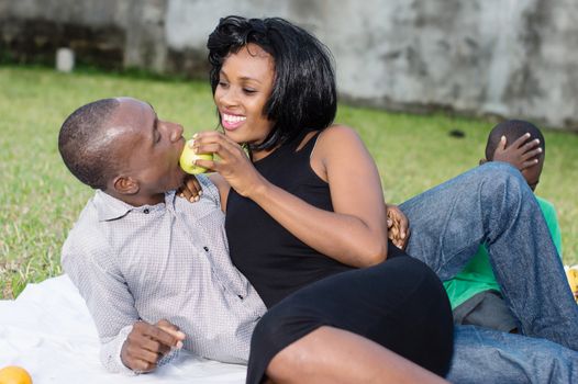 happy couple sitting at the park with their son and eating a green apple in love