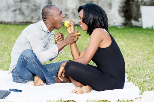 young couple sitting on the grass sharing a green apple together lovingly