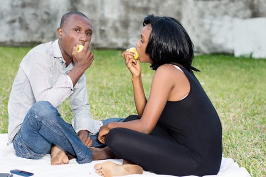 young couple sitting on the grass eating a green apple together