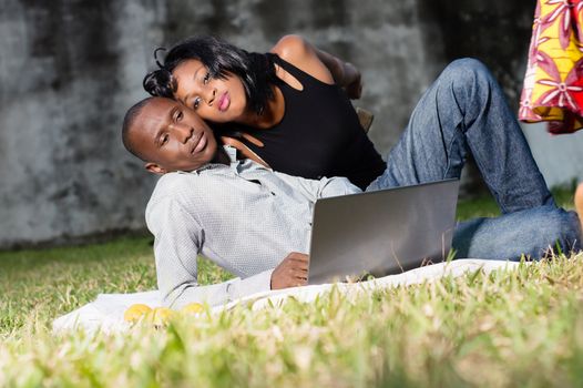 young happy couple lying in love at the park and using a laptop