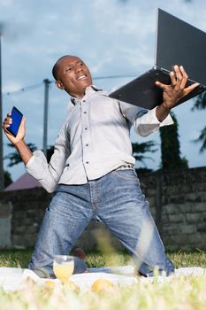 Young man kneeling in park with laptop in hand Cry of joy