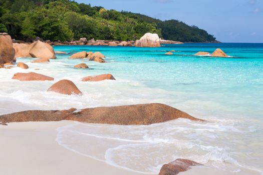 Beach with blue water and blue sky and white sand and some rocks