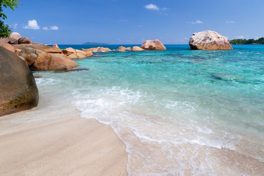 Beach with blue water and blue sky and white sand and some rocks