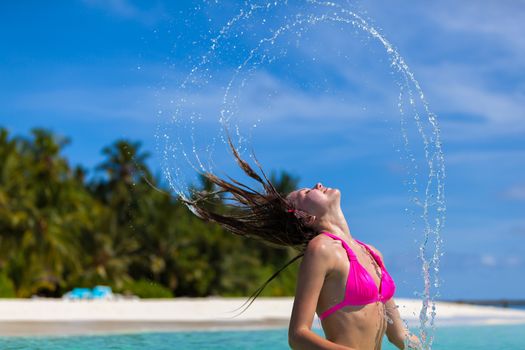 young woman is standing in the water and throwing her hair back