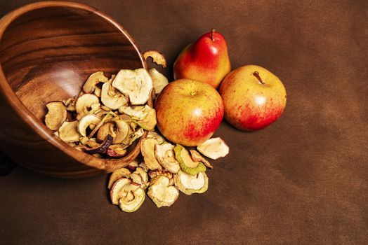 Pile of dried apples together with two whole apples and one pear lying in a wooden bowl. Still life concept of fall season harvest and homemade fruit processing