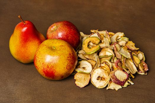 Pile of dried apples together with two whole apples and one pear. Still life concept of fall season harvest and homemade fruit processing