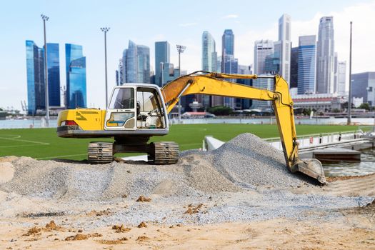 Excavator parked on the mound in the city with skyscraper background.