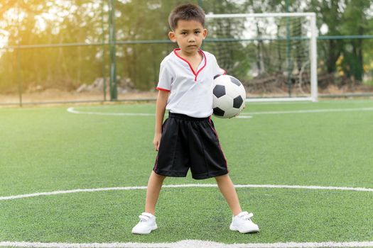 Asian boy holding a football on the football field.