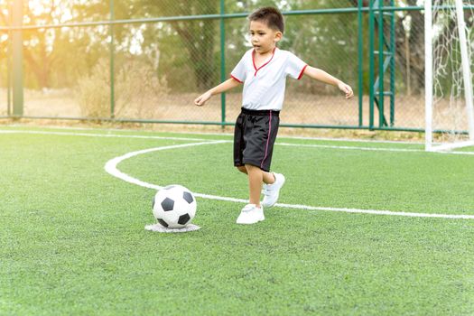 Asian boy playing soccer in the artificial grass field.