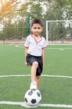 Asian boy playing soccer in the artificial grass field.