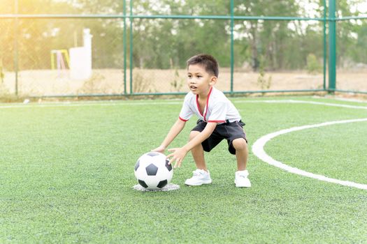 Asian boy playing soccer in the artificial grass field.