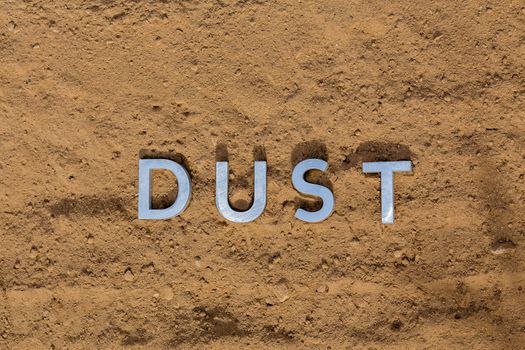 the word dust laid with silver metal letters on dusty road surface - close-up flat lay perspective under direct sunlight