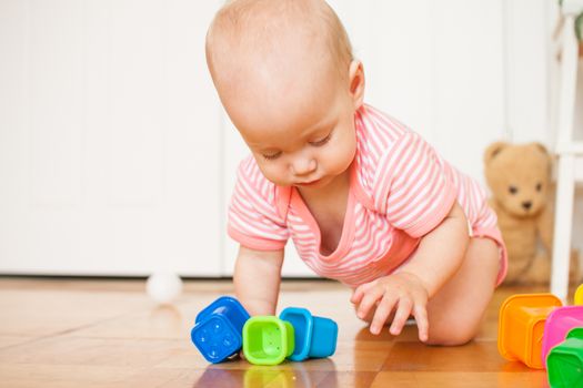 Little baby girl sitting on the floor, crawling and playing with brightly colored educational toys, pyramids