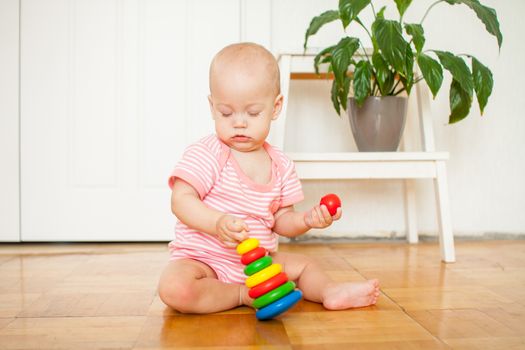 Little baby girl sitting on the floor, crawling and playing with brightly colored educational toys, pyramids