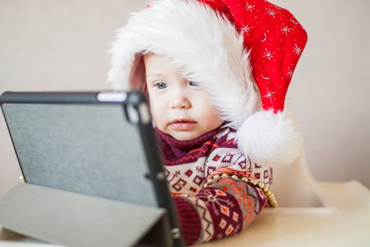 Little baby girl in Santa Claus hat looks at the tablet screen. Talk with family, Happy New Year and Merry Christmas.