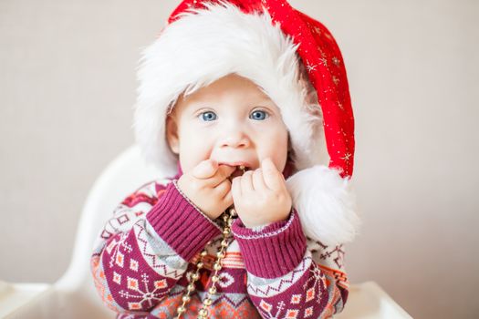 A little baby girl in a New Year's hat of Santa Claus examines and plays with New Year's decorations. Merry Christmas and Happy New Year greetings.