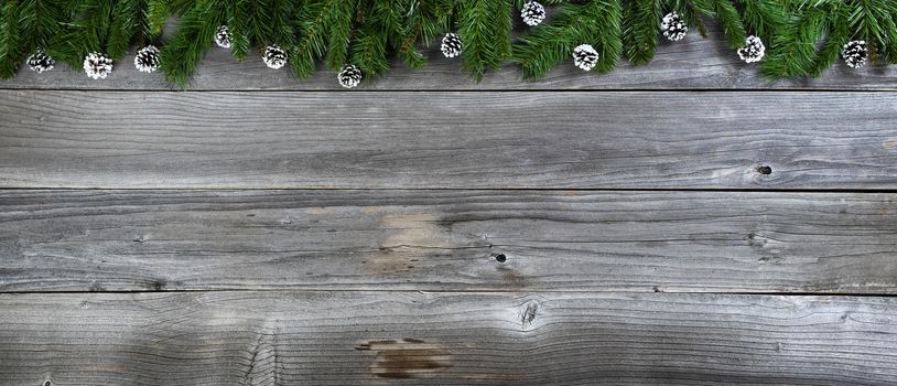 Merry Christmas and Happy New Year concept with pine cone ornaments inside of fir branches on rustic wooden boards 