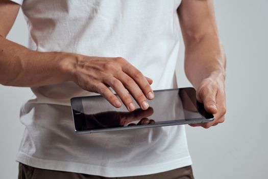 Tablet with a touch screen on a light background male hands white t-shirt cropped view. High quality photo