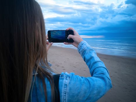 beautiful alone girl on the beach. Girl looking at stormy sea and taking a picture with smarphone. The spectacular Storm with rain Is Coming in Estonia. Baltic sea