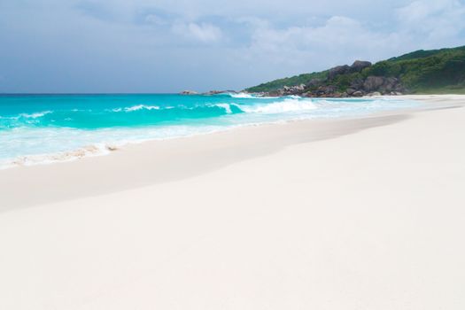 White sand beach with some waves and blue sky in the far a hill with green plants