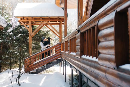 couple of young people a guy and a girl on the porch of a snow-covered wooden house in the winter mountains