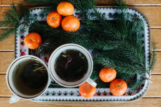two cups of herbal tea on a table with tangerines and a spruce branch on christmas eve