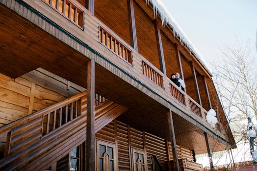 couple of young people a guy and a girl on the porch of a snow-covered wooden house in the winter mountains