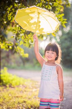 happy little girl with umbrella walking in the park on sunny day