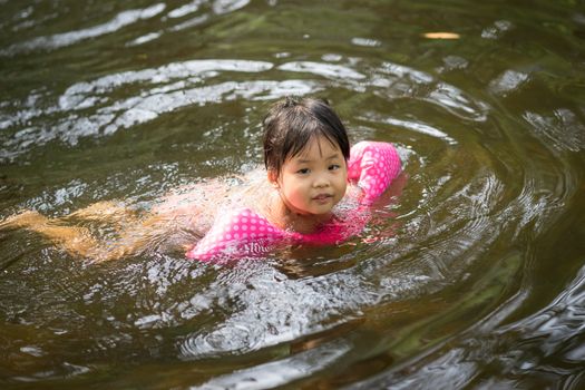 little asian girl wearing inflatable sleeves swimming in nature water on holiday