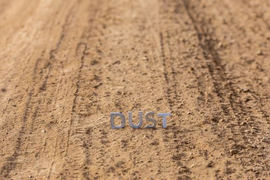 the word dust standing on dusty road surface in linear perspective with selective focus and background blur under direct sunlight