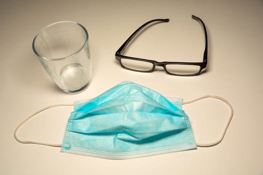 Surgical blue mask, glasses and an empty glass, top view