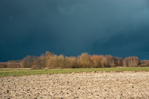 Ploughed field, autumn forest and dark big cloud on the sky