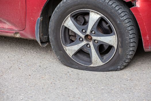old red civil car flat tire close-up at dry sunny day on gray asphalt surface.