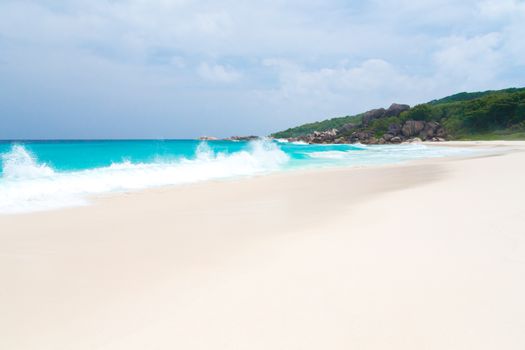 White sand beach with some waves and blue sky in the far a hill with green plants