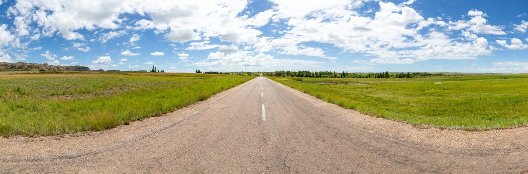 The straight asphalt road with meadows on both sides