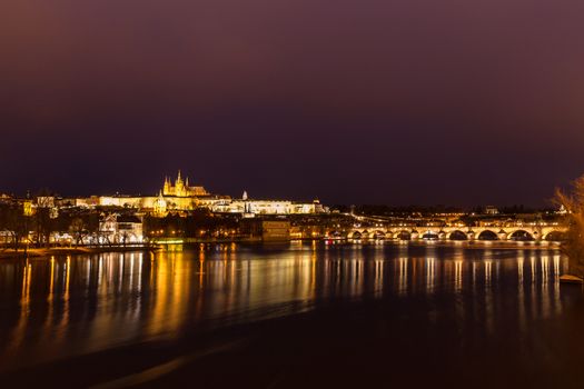 Panorama night view of the light illuminated Prague Castle and St. Vitus Cathedral with Charles Bridge over Vltava River and in the center of old town of Prague, Czech Republic