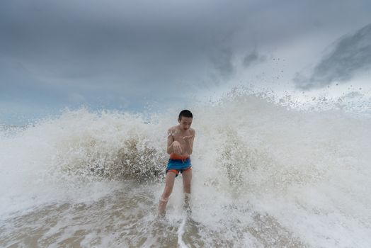 An Asian boy has felt happy and fun on the beach with a cloudy sky.