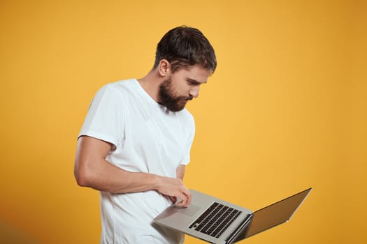 A man with a beard holds a laptop in his hand on a yellow background keyboard monitor new technologies side view. High quality photo