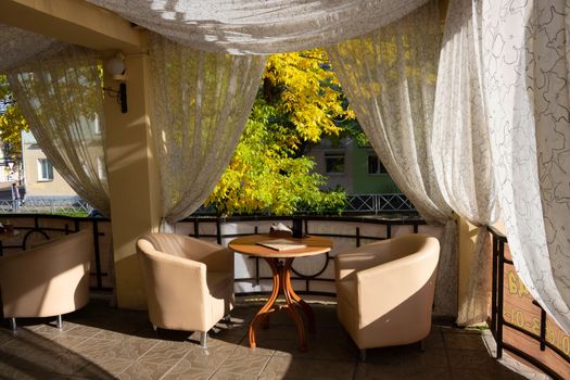 Summer stylish outdoor cafe with leather chairs and white curtains.